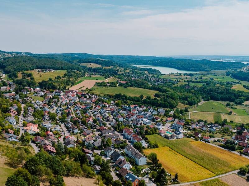 Luftaufnahme von Güttingen, umgeben von Wäldern und Feldern und in der Ferne der Bodensee.