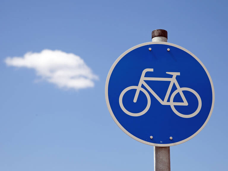Ein blaues Verkehrsschild mit einem weißen Fahrradsymbol, vor einem klaren Himmel mit einer einzelnen weißen Wolke.