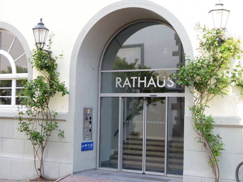 Der Eingang mit der Aufschrift "Rathaus" über einer Glastür, eingerahmt von zwei Laternen und Rosen.