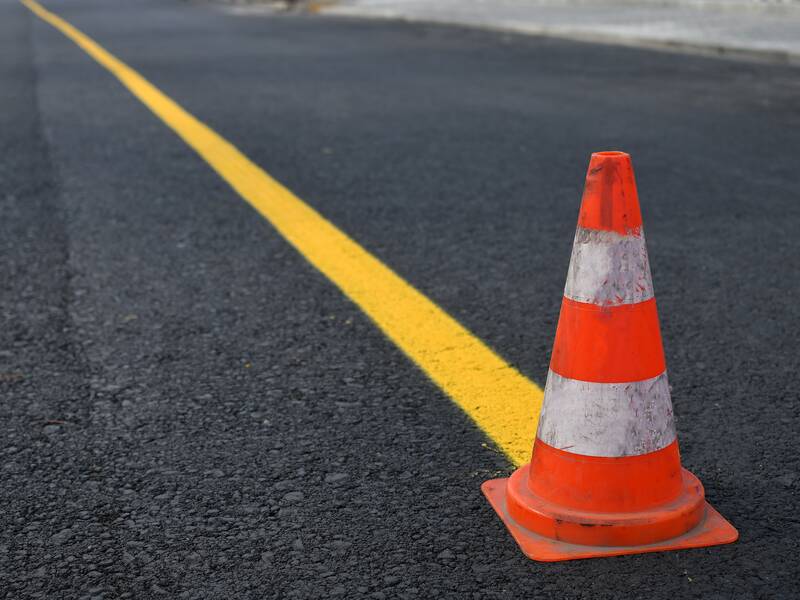 Ein oranges Verkehrshütchen steht auf einer Asphaltstraße neben einer gelben Linie.