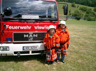  Zwei Kinder stehen in Feuerwehruniformen vor einem Feuerwehrauto 