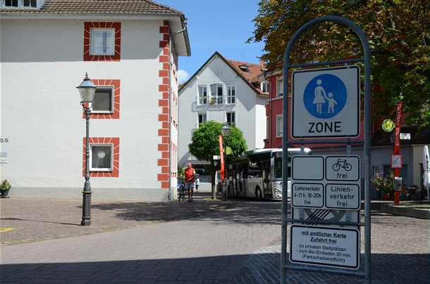  Fußgängerzone mit entsprechendem Schild im Vordergrund, im Hintergrund sieht man einen Passanten und einen Bus der eine Bushaltestelle anfährt 